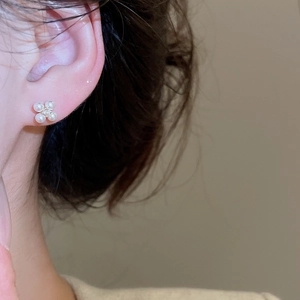 Detailed close-up of gold-plated clover pearl stud earrings on a model's ear