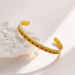 Detailed shot of golden open bangle with colorful enamel leaf pattern on a white rock