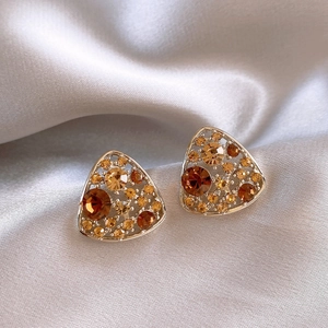 Macro detail of triangle drop earrings with amber rhinestones on champagne silk fabric