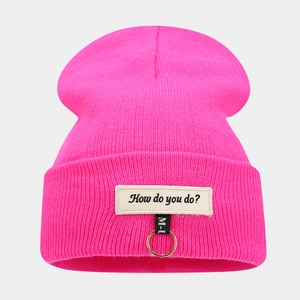 Détail du bonnet en maille rose vif avec anneau métallique et écusson brodé