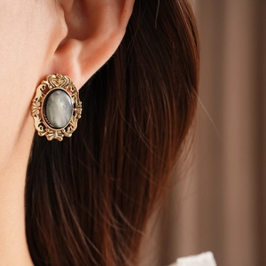 Close-up of vintage golden oval resin earring with intricate metal carving on model