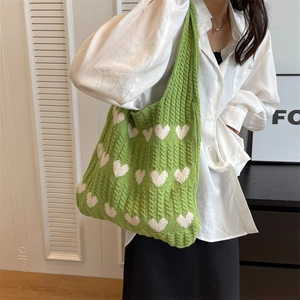 Detailed knit texture of green crochet shoulder bag with white heart patterns