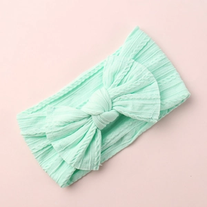 Macro detail of mint green knitted bow headband with textured cable stitch pattern