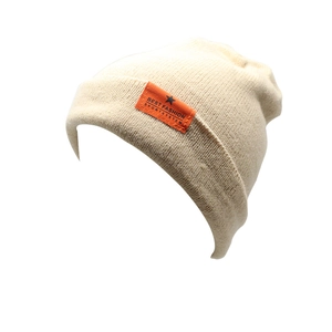 Close-up of fine knit beanie texture with orange star brand label on off-white fabric