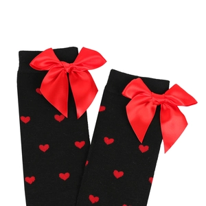 Close-up of black knit over-the-knee socks with red heart patterns and satin bows