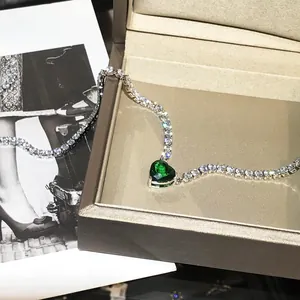 Macro shot of heart-shaped emerald green pendant on sparkling tennis chain with jewelry box