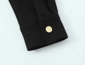 Détail d'une manche de robe noire avec un bouton doré rond et une texture sergée
