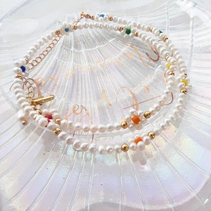 Close-up of baroque pearl necklace with colorful floral beads on a summer scallop plate