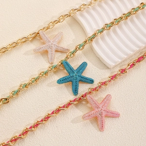 Detailed view of woven starfish pendant necklaces in blue pink and white colors on sand