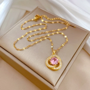 Detail of gold floral pendant necklace featuring a pink stone on a beige box