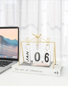 Creative gold bird flip calendar detail showing metallic frame and date cards on desk