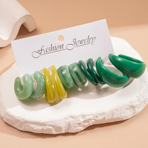 Detail of five pairs of resin C-shaped hoop earrings in various gradient green marble patterns