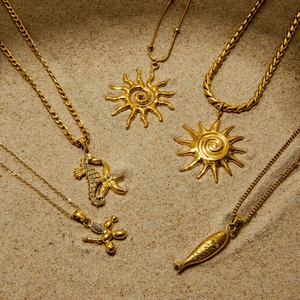 Detailed view of gold stainless steel necklaces with sun and seahorse pendants on beach sand