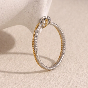 Detail of two-tone 18K gold plated stainless steel twisted knot ring on white ceramic