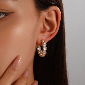 Elegant gold-tone hoop earrings with rectangular cubic zirconia stones worn by a model
