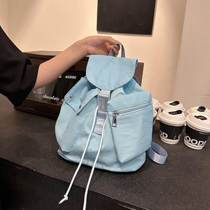Detail of light blue nylon backpack featuring front zip pockets and buckle closure