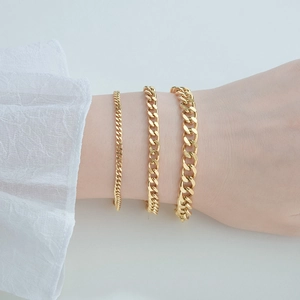 Close-up of three 18k gold-plated Cuban link chains in different widths on a female wrist