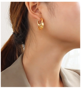 Detail of gold-plated hoop earrings with five dangling sequins worn by a model