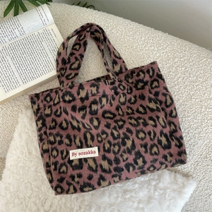 Detailed view of leopard print plush handbag with brand tag on soft white wool background