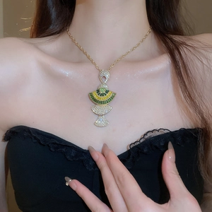 Close-up of a gold necklace featuring fan and fishtail pendants with colorful gemstones