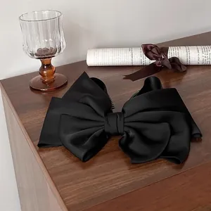 Detailed close-up of a large black satin bow banana clip on a vintage wooden surface