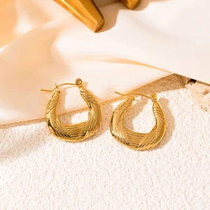Macro shot of gold hoop earrings with horizontal texture on ivory silk and stone background