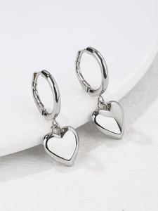 Detailed view of shiny silver hoop earrings with 3D heart charms on a white tray