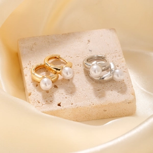Elegant gold and silver hoop earrings with round pearls on a textured stone surface