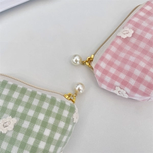 Detail of checkered makeup pouch with daisy embroidery and elegant pearl zipper pull