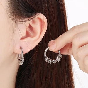 Close-up of silver hoop earring with hollowed patterns and bead on ear lobe