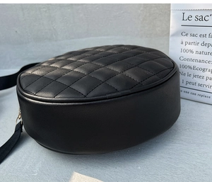 Detail of round black quilted PU leather shoulder bag with metallic buckle and strap