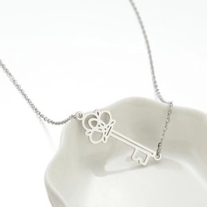 Collar de llave de acero inoxidable con colgante de corona sobre un cuenco de flores blanco
