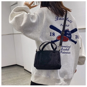 Model wearing a small black corduroy Boston bag with shoulder strap in a casual indoor setting