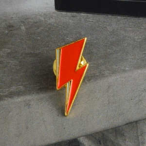 Detailed view of red lightning bolt enamel pin with gold plating and blue accents