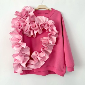 Détail du sweat à col rond avec un cœur à volants en satin rose sur tissu rose vif