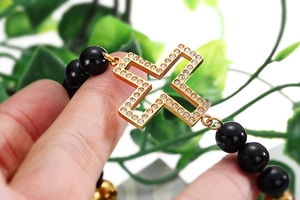 Close-up of black beaded bracelet with gold cross pendant and white zircon inlay