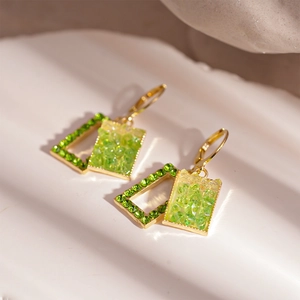 Detail view of gold leaf earrings featuring green rhinestones and stone texture on white rock