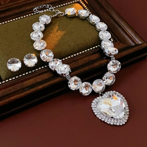Detail of luxury crystal heart pendant necklace and stud earrings set on green velvet padding