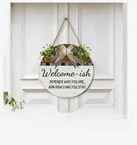 Detail of Welcome-ish wooden sign featuring a grey bow, greenery, and rustic hemp rope