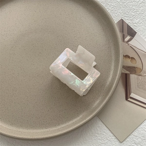 Dettaglio della pinza per capelli bianca iridescente su vassoio minimalista in ceramica