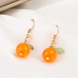 Detail shot of orange fruit earrings with green leaf charm on white silk fabric