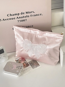 Detail of pink satin makeup bag with white embroidered bow and pearl zipper pull