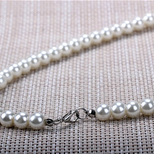 Detail of white round pearl necklace featuring a polished silver lobster clasp closure