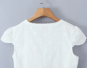 Close-up of intricate hollow embroidery and lace details on white V-neck top