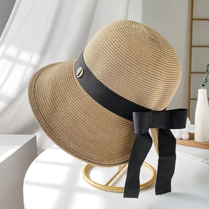 Elegant beige straw sun hat with black ribbon bow on a minimalist gold stand