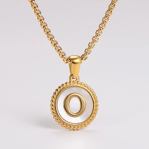 Macro shot of gold pendant with white shell inlay and 3D letter O on metal chain