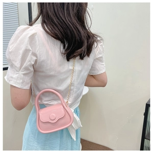Pink mini jelly bag with golden chain strap worn by a model against a clean wall