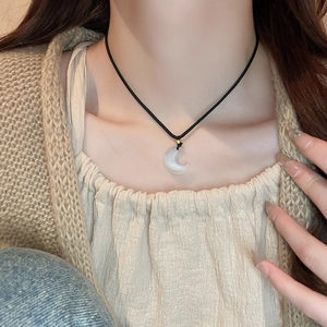 Macro view of a sun and moon pendant necklace on a black faux leather cord over knitwear