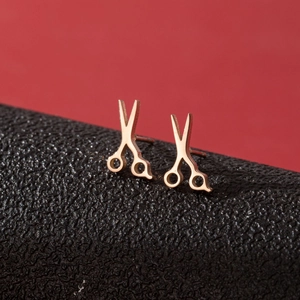 Macro shot of rose gold scissors-shaped stud earrings on a textured black leather background