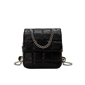 Detail of black quilted leather backpack featuring silver chain and heart ornament